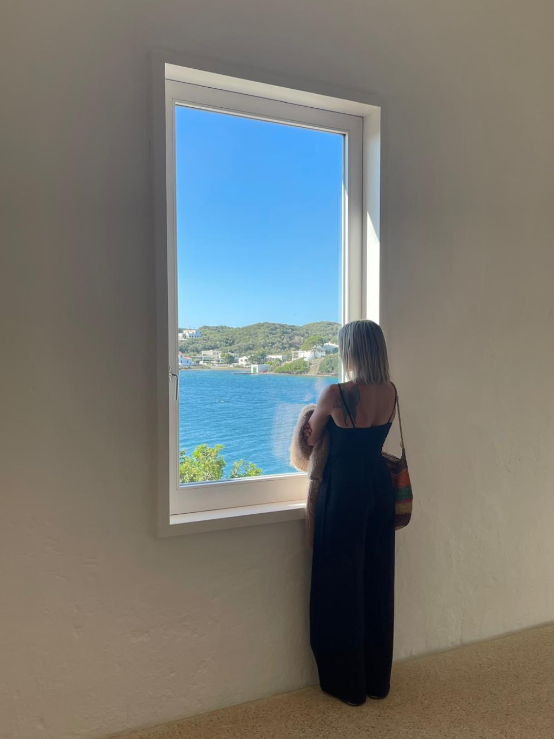 Natalia Palmieri mirando el mar por una ventana en Illa del Rei, Menorca